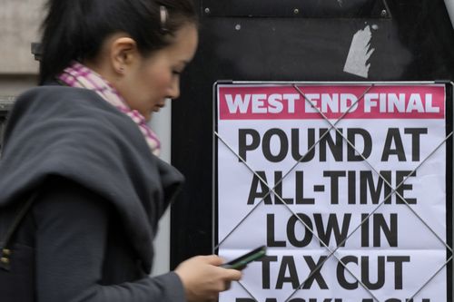 A woman walks past a headline posted on a wall in London, Tuesday, September 27, 2022. 