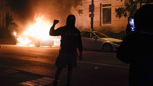 A demonstrator is filmed in front of a burning car during a protest of the death of George Floyd.