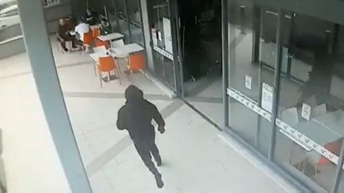 The gunman, dressed in black, runs up behind Wally Ahmad. (9NEWS)