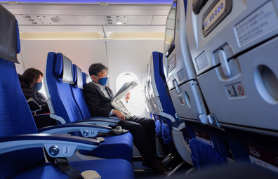 A passenger wearing a face mask seen reading a news paper inside the ANA plane