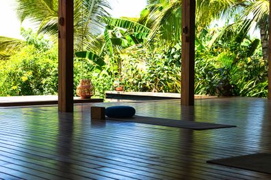Open tropical yoga studio place with view outside to the beautiful garden with palm trees and ocean. Holiday concept.