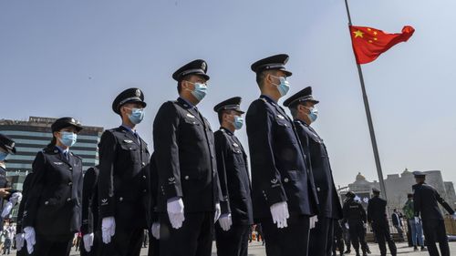 Chinese police officers wear protective masks as they stand in formation next to a national flag at half staff just before three minutes of silence to mark the country's national day of mourning for COVID-19