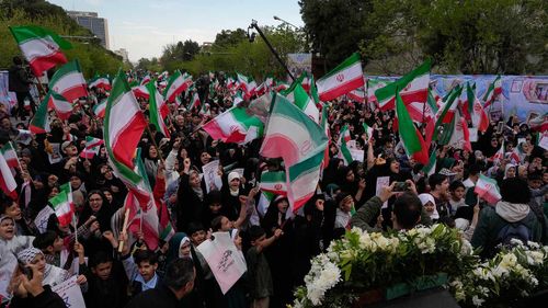People wave Iranian flags and chant slogans in a memorial for school children killed in a US missile strike.