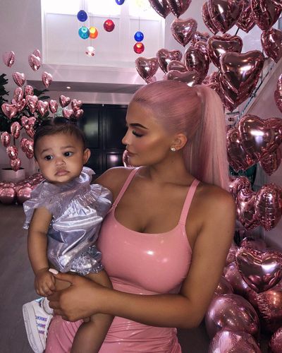 Kylie matches pink hair and balloons with a shiny pink latex suit while holding daughter Stormi.