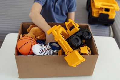 Boy preparing cardboard donation box full with toys. Concept of volunteering work, donation and clothes recycling. Helping poor people. Little boy holding card box with his old toys inside. Donation concept.