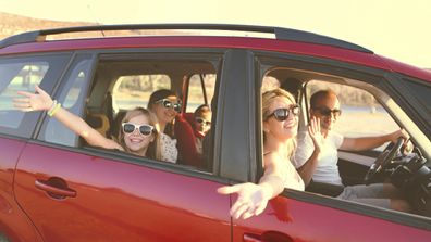 Happy smiling family with daughters in the car with sea background. Portrait of a smiling family with children at beach in the car. Holiday and travel concept.