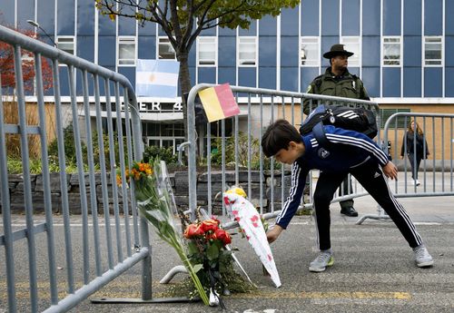 A boy places flowers at a makeshift memorial which includes Argentinian and Belgian flags . (AAP)