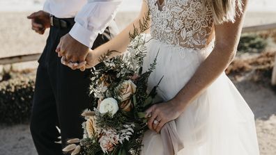 Close-up of bride and groom walking on path at the coast