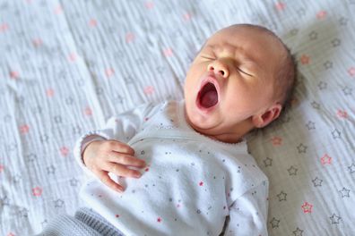 Adorable newborn baby girl sleeping and yawning in bed at home