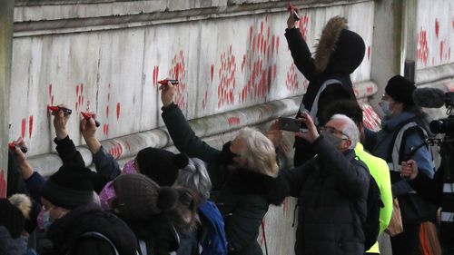 People paint red hearts onto the COVID-19 Memorial Wall mourning those who have died, opposite the Houses of Parliament on the Embankment in London.