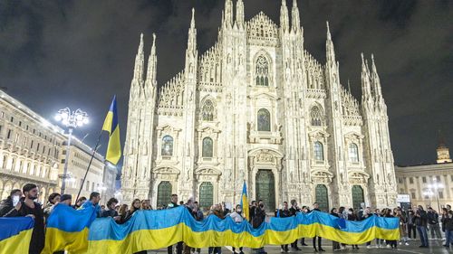 People hold a large flag of Ukraine in Duomo Square, Milan, Italy, Thursday Feb. 24, 2022.