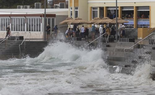 People flock to a waterfront cafe as wild seas pound Cronulla esplanade on Saturday morning.