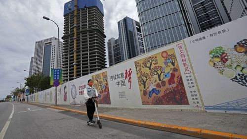 Una ragazza che indossa una maschera per proteggersi dal coronavirus, guida una moto attraverso la propaganda del governo cinese "Sogno cinese" Un cartellone è esposto lungo l'edificio degli uffici commerciali in costruzione a Tongzhou, un sobborgo di Pechino.