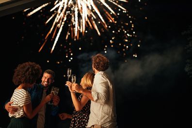 New Year's party Four friends standing outside, toasting with glasses of wine and watching fireworks