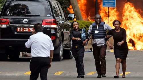 Bystanders are helped to ssfety as cars burn outside the DusitD2 hotel complex in Nairobi.