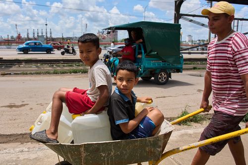 A man carries containers of water with his children in Havana, Cuba.