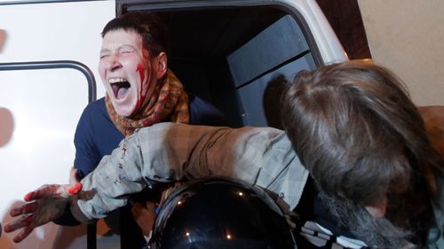 A blood-soaked protester is detained in St Petersburg on Vladamir Putin's 65th birthday. (AP)