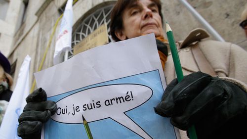 A woman holds a pencil and a poster reading in French "Yes, I am armed" during a rally in support of Charlie Hebdo, a French satirical weekly newspaper that fell victim to a terrorist attack, in front of the French Consulate in Milan, Italy. (AAP)