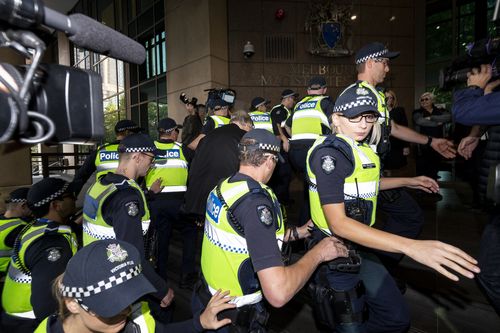 Police swarm the Cardinal as he walks up the steps of the Melbourne Magistrates' Court. 