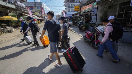 A group of travelers cross the road with their luggage in Vang Vieng, Laos.