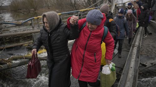 Women hold hands while crossing the Irpin river on an improvised path under a bridge that was destroyed by a Russian airstrike, while assisting people fleeing the town of Irpin, Ukraine, Saturday, March 5, 2022. What looked like a breakthrough cease-fire to evacuate residents from two cities in Ukraine quickly fell apart Saturday as Ukrainian officials said shelling had halted the work to remove civilians hours after Russia announced the deal. (AP Photo/Vadim Ghirda)