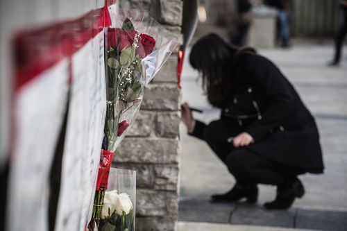 A woman writes her condolences on the memorial strewn with floral tributes. Picture: AP