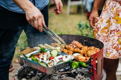 A close up of  aman cooking different foods on a barbecue.