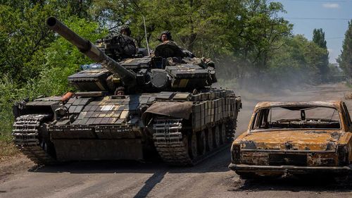A Russian tank rolls past the wreckage of a car in Ukraine.