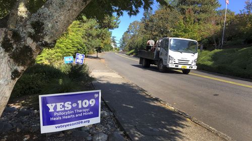 A truck drives past a sign supporting a ballot measure that would legalise controlled, therapeutic use of psilocybin mushrooms. War veterans with PTSD, terminally ill patients and others suffering from anxiety are backing the ballot measure.