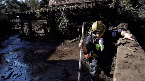 Alex Broumand of the Montecito Fire Department walks in mud in front of homes damaged from storms. (Image: AAP)
