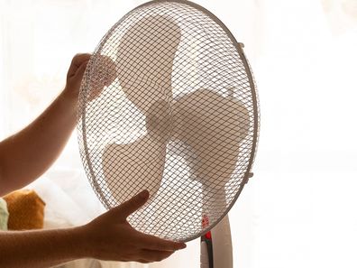 Man holding floor fan with hands at home in bedroom on hot day in summer