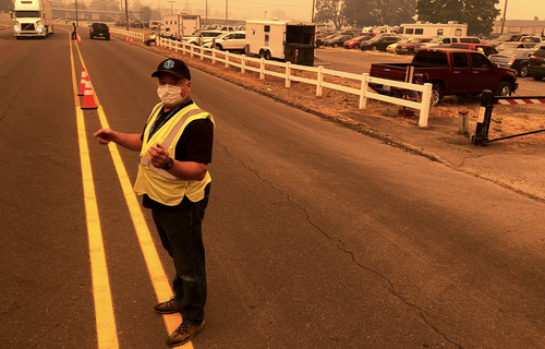 Under a smoke-filled sky, volunteer Shawn Daley directs traffic into the parking lot an evacuation center at the Oregon State Fairgrounds, which was crowded with hundreds of cars, pickup trucks and campers of evacuees, in Salem on Tuesday, Sept. 8, 2020. 