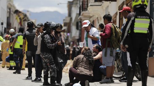 Police talks to people next to the site where a car was crushed by debris after an earthquake shook Cuenca, Ecuador, Saturday, March 18, 2023.