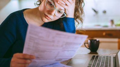 Young brunette curly female reading her bill papers, looking stressed