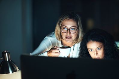 Two women looking at a computer screen late at night.