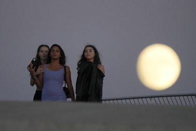 Girls stand on the roof of Lisbon's Museum of Art, Architecture and Technology as a nearly full moon rises in the background, Tuesday, Aug. 29, 2023.  