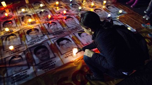 A woman places a candle on photos of the missing students during a protest against the disappearance of 43 students from the Isidro Burgos rural teachers college, in Mexico City, Wednesday, Oct. 22, 2014. Tens of thousands marched in Mexico City's main avenue demanding the return of the missing students. 