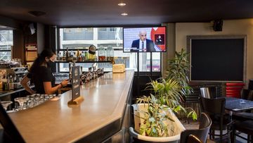 A waitress wearing a protective mask watches a TV showing Swiss Interior and Health Minister Alain Berset at a press conference in Bern announcing new measures against the Coronavirus (COVID-19), inside of the &quot;Les Boucaniers&quot; in Lausanne, Switzerland, Friday, Dec. 18, 2020