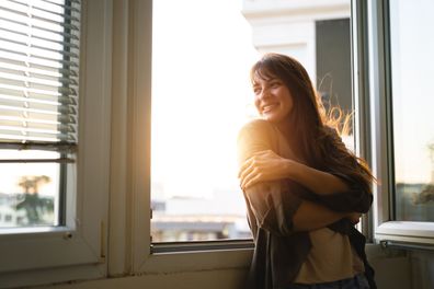 Young woman looking through the window while enjoying fresh air.