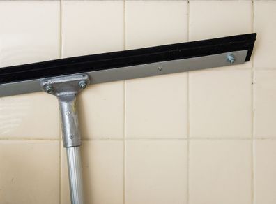 Long squeegee with metal handle near the wall of storage room.