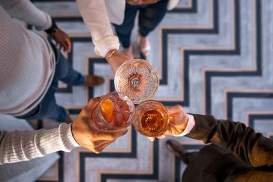 A high angle shot of an unrecognisable multi-ethnic group of friends wearing smart-casual clothing in a bar in Newcastle Upon Tyne. They are all making a celebratory toast with cocktails.