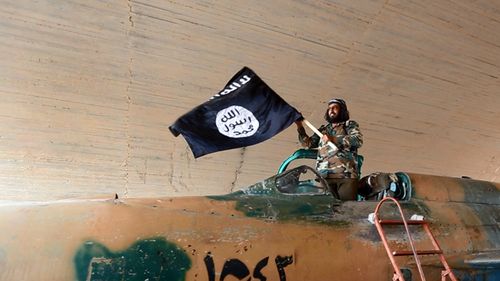 An Islamic State fighter (thought to be 2014) waving their flag from inside a captured government fighter jet following the battle for the Tabqa air base in Raqqa, Syria. (AAP)