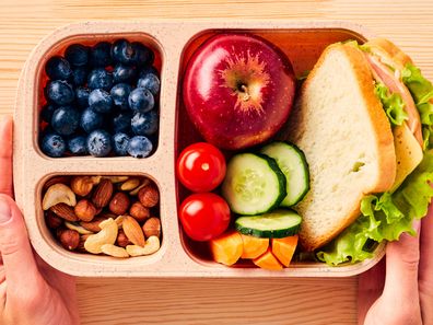 Women's hands hold lunchbox of healthy food over wooden table.