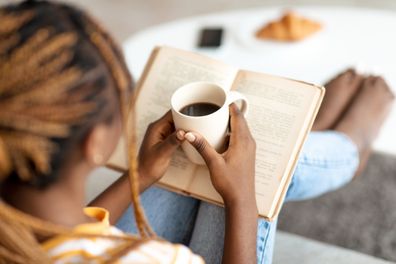 woman sitting on couch at home, reading book, drinking coffee, enjoying weekend alone, copy space, back view