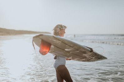 Australian bride and groom surf together before beach wedding