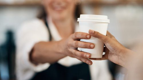 Cropped shot of a barista handing a customer a cup of coffee at a cafe