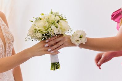 A bridesmaid hands a delicate bouquet of white roses, eustoma, and baby's breath to the bride. The shot captures only their hands and the elegant wedding flowers, symbolizing a touching wedding moment.