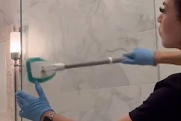 Professional cleaner scrubs a shower glass door