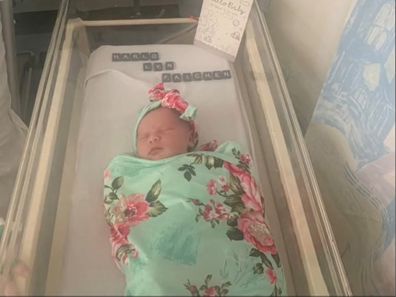 Newborn baby wrapped in floral blanket lying in bassinet at the hospital.