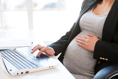 Cropped image of pregnant businesswoman typing something on laptop while sitting at her working place in office